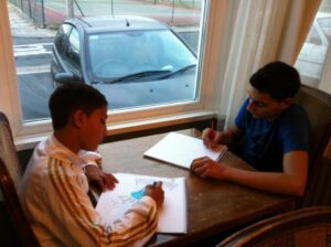 Two boys seated at table drawing