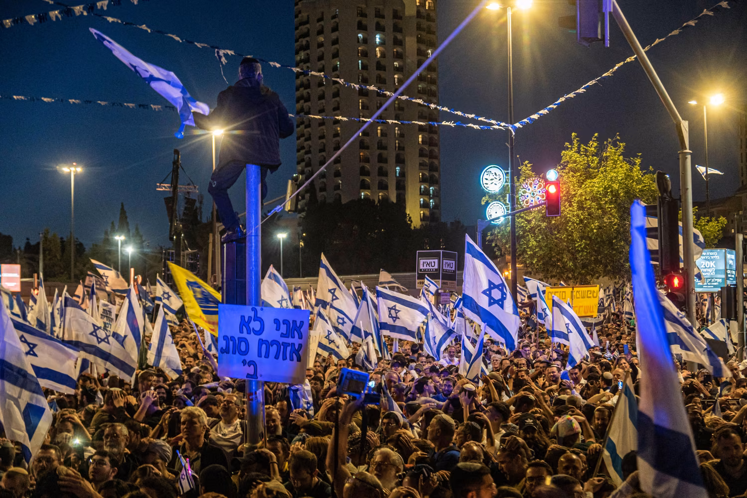 Crowds in a street waving Israeli flags and placards.