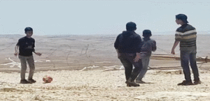 children playing football on very dry ground with hills in the background