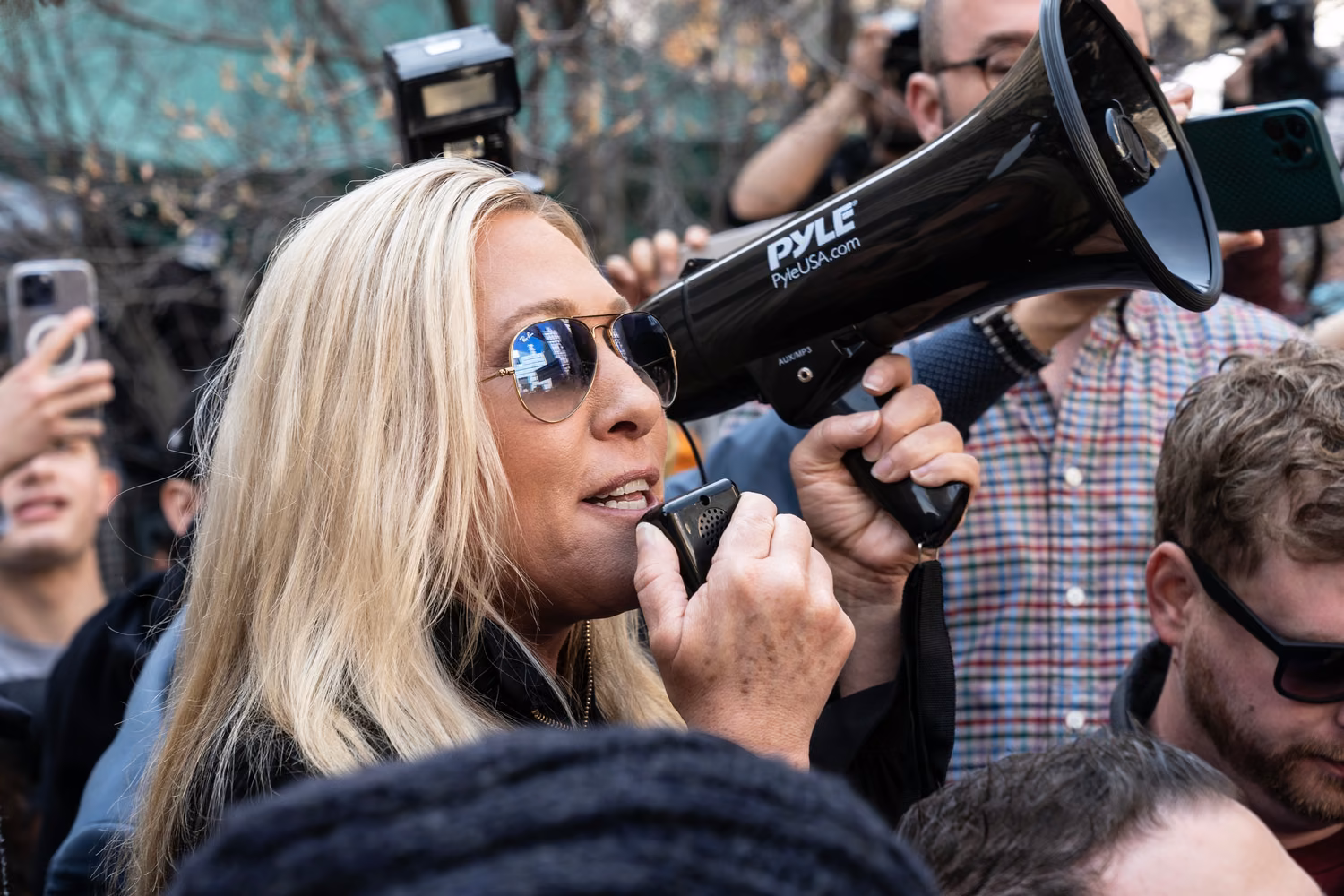 Blonde woman wearing dark glasses speaks into a megaphone